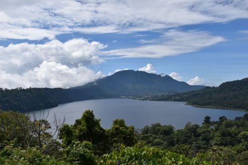 Uitzicht op een van de Twin Lakes op Bali, omringd door groene bergen en tropische bossen onder een blauwe lucht met wolken