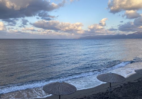 strand op Kreta met parasols aan zee met bergen op de achtergrond bij zonsondergang